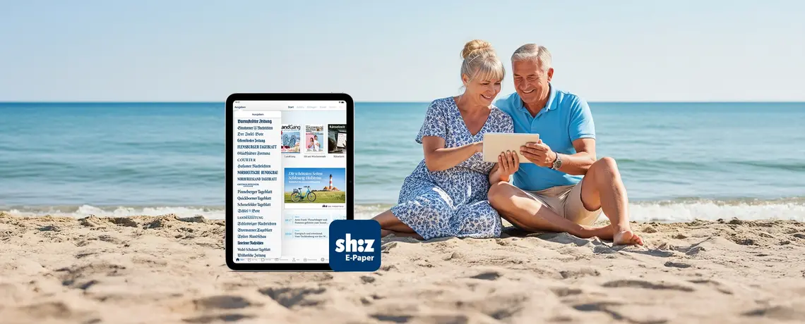 Älteres Pärchen sitzt am Strand und ließt auf einem Tablet