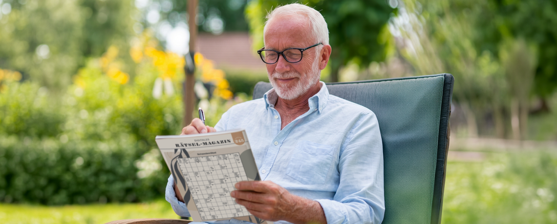 Mann sitzt im Garten und füllt Rätsel aus