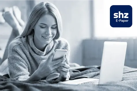 Junge Frau liegt auf einem Bett und liest auf ihrem Smartphone die digitale Zeitung in der App shz E-Paper