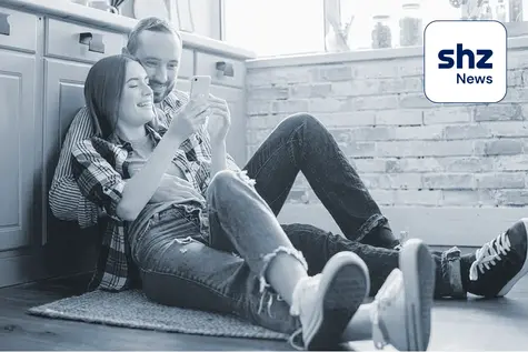 Junges Pärchen sitzt auf dem Boden und liest auf dem Smartphone die App shz News